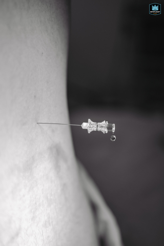A black and white photograph captures a needle inserted into a delivering mother's back in Pernambuco, Brazil, with a drop of anesthesia seen falling.